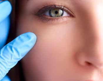 Beautician doctor hands in gloves touching female face. Upper eyelid reduction, double eye lid removal plastic surgery concept. Ophthalmologist or oculist checks healthy vision in green eyesight.