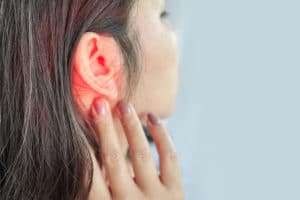 woman suffering from ear pain , her ear is highlighted red. 