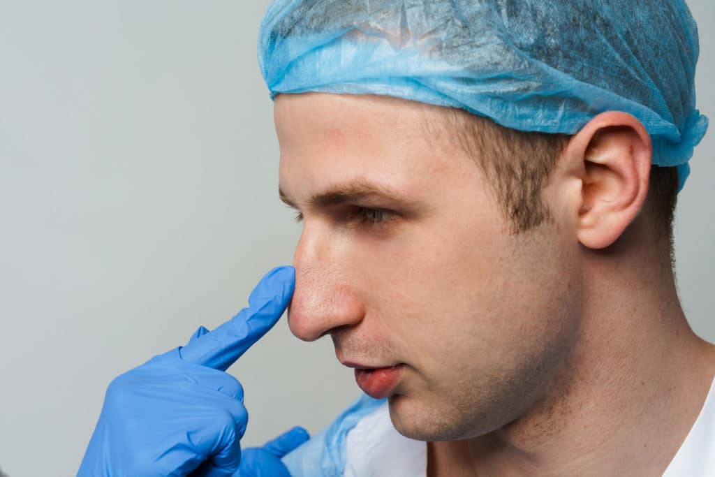 Doctor touches man nose on consultation, inspecting it prior to performing a septoplasty.