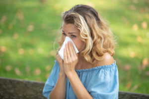 Woman blowing her nose, experiencing allergies while outside